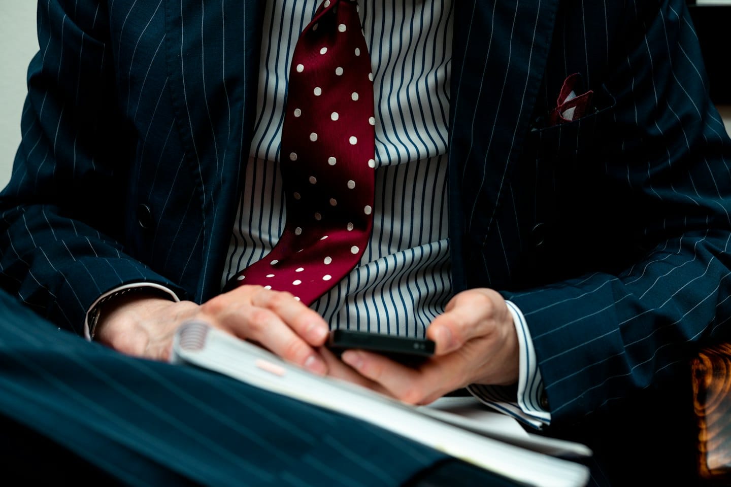Man in pak met smartphone en open notitieboek.