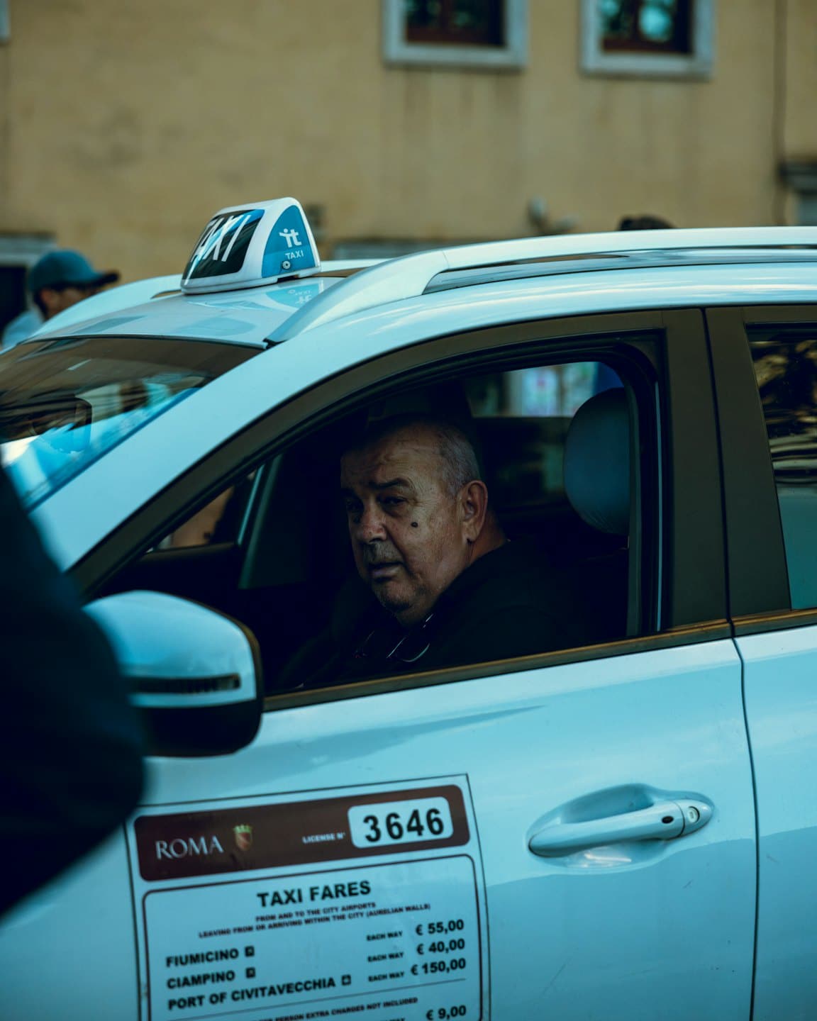 Taxichauffeur kijkt uit de bestuurdersstoel van een witte taxi.