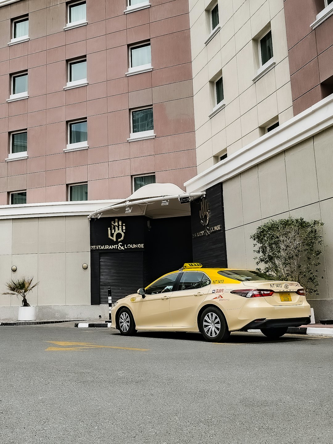Gele en beige taxi geparkeerd voor een restaurant met betegelde gevel.