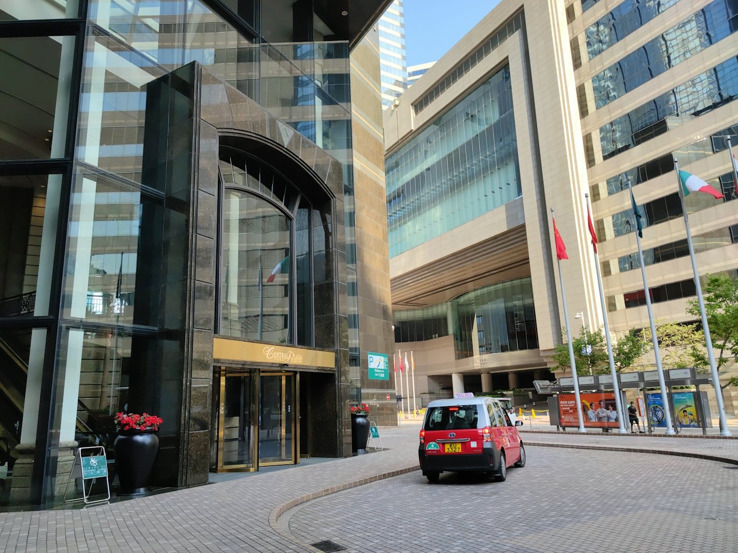 Een rode taxi stopt bij de ingang van een modern hoogbouwgebouw.